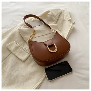 Brown leather crescent bag with gold horseshoe buckle next to a smartphone for size scale