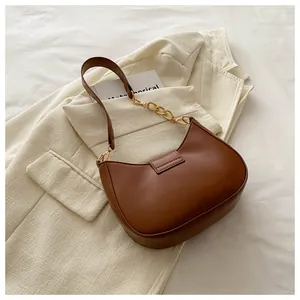 Detail of a brown half-moon underarm bag with gold chain and refined faux leather texture