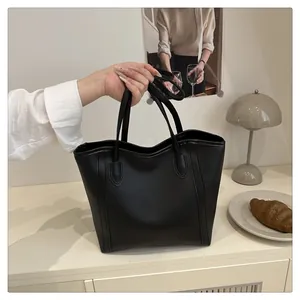 Detail shot of the matte black leather tote bag held by hand in a cozy indoor setting