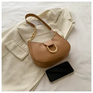 Detail of camel crescent shoulder bag with gold D-buckle and chain strap next to a phone