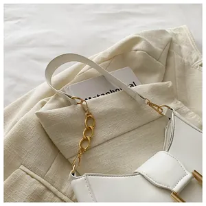 Close-up of white leather underarm bag with gold chain on a beige blazer background