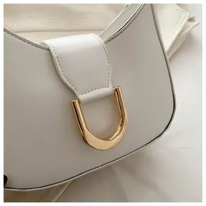 Detail of white leather shoulder bag featuring a polished gold U-shaped buckle and stitching