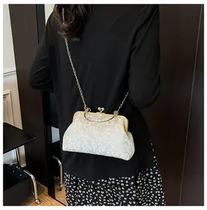 Détail de broderie florale beige sur sac à fermoir rétro avec bandoulière dorée
