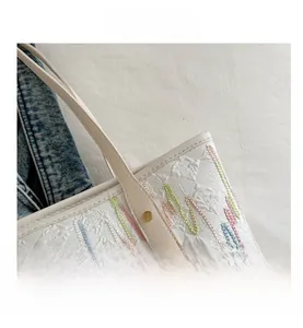 Detail of white tote bag with colorful wave embroidery and leather logo patch