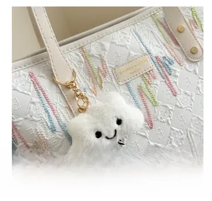 Detail of white quilted tote bag with colorful embroidery and plush cloud charm