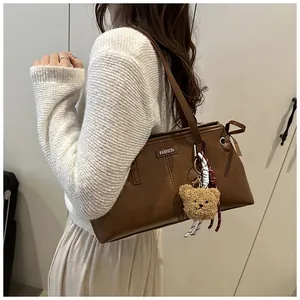 Bolso tote de cuero marrón con colgante de osito de peluche y logotipo metálico