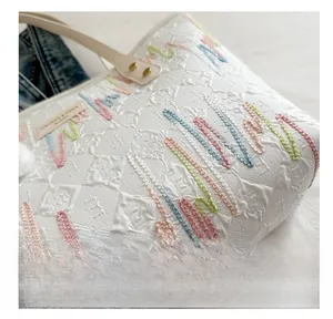 Detailed close-up of quilted cream tote bag featuring colorful wavy embroidery and metal buckles