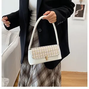 Detailed shot of a white leather underarm bag with a golden tweed fabric flap and metal lock