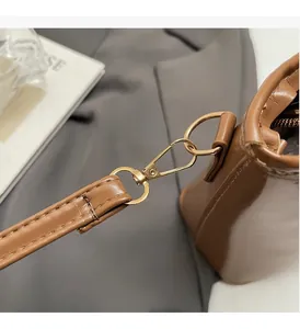 Dettaglio del gancio in metallo dorato e della tracolla in pelle su una borsa marrone