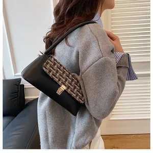 Close-up of minimalist black leather shoulder bag with textured tweed flap and gold clasp