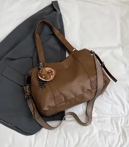 Close-up of brown faux leather tote bag with wide patterned strap and plush charm detail
