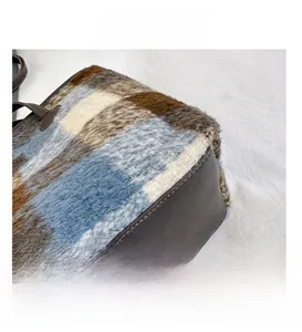 Detailed close-up of plaid plush fabric and brown leather stitching on women's tote bag