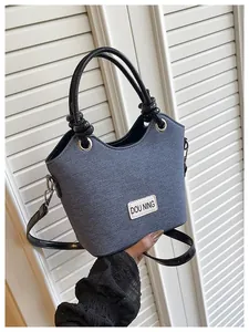 Détail de la texture denim bleu et de l'anse noire nouée de ce sac seau moderne