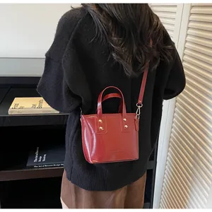 Dettagli della borsa a secchiello in vernice rosso scuro con rivetti in metallo e tracolla