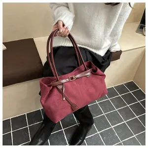 Detail of burgundy suede tote bag with brown leather handles and decorative metal buckle