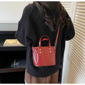 Dettaglio di borsa tote rossa lucida con rivetti dorati e tracolla rimovibile