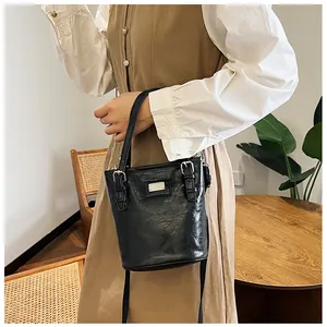 Detail of a black shiny bucket bag with metal plaque shown in a lifestyle setting
