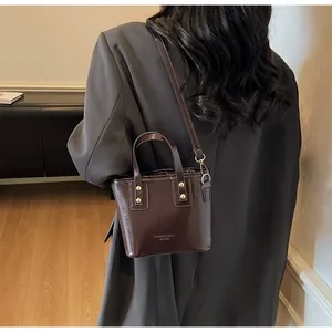 Dettaglio di una mini borsa in pelle lucida marrone scuro con borchie dorate e tracolla