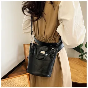 Model wearing dark vintage bucket bag with adjustable buckle strap and silver plate detail