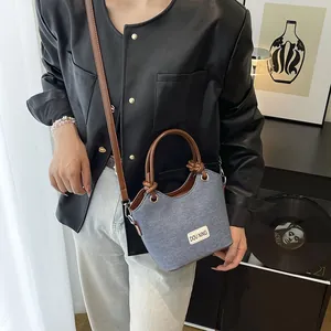 Petit sac seau en jean bleu avec anses en cuir marron pour femme présenté en scène de mode