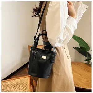 Model wearing a black glossy oil wax leather bucket bag with silver metal details