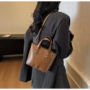 Borsa a secchiello in pelle marrone indossata da una modella in un interno moderno