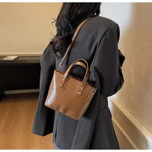 Vista posteriore di una modella con la borsa a tracolla in pelle marrone con doppi manici e borchie