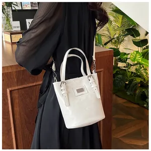 Detail of white bucket bag with metallic logo plate and adjustable shoulder straps