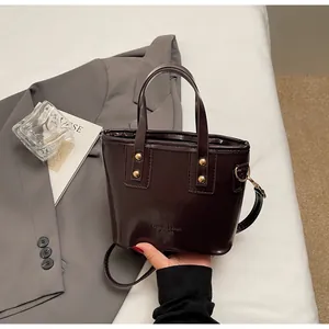 Dettaglio borsa tote in pelle marrone scuro lucida con rivetti dorati e tracolla