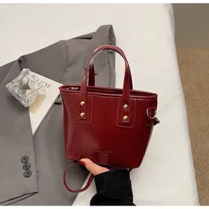 Dettaglio borsa a mano in pelle bordeaux con borchie dorate e tracolla regolabile
