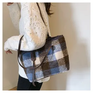 Close-up of a blue plaid wool tote bag worn over the shoulder with a leather tag