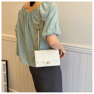 Detail of white quilted crossbody bag with gold chain strap and spherical buckle adjuster
