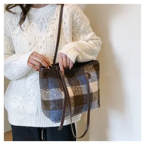 Detail of plaid wool tote bag featuring brown leather straps and fashion label patch