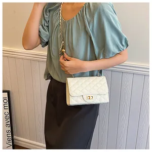 Detail of white quilted crossbody bag with golden turn-lock and chain strap with ball buckle