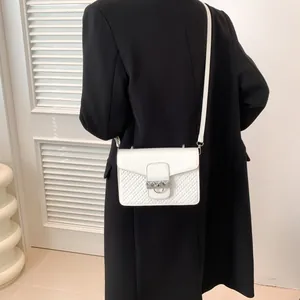 Retro white crossbody bag with quilted texture and silver metal ring buckle worn over a black blazer