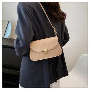 Sacoche beige avec boucle en métal doré portée par un mannequin en veste de blazer