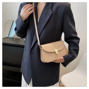 Mannequin portant un sac selle minimaliste abricot en cuir avec boucle dorée sur un blazer