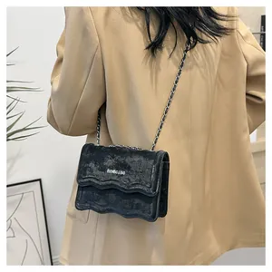 Detail of black crossbody bag with wavy flap edge and chain strap on female model