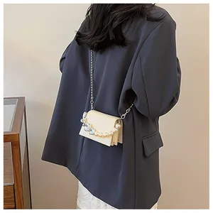 Gros plan d'un mini sac bandoulière crème avec breloque cœur et chaîne en perles fantaisie