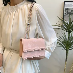 Pink velvet crossbody bag with wavy flap design and elegant silver chain strap