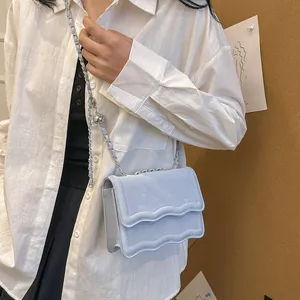 Light blue crossbody bag with wavy flap and silver chain strap shown on a model