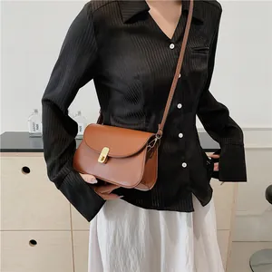 Sacoche marron en cuir avec boucle dorée portée en bandoulière pour un look élégant