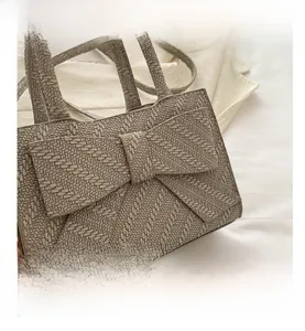 Close-up of beige woven texture handbag featuring a large decorative bow and top handle