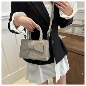 Detail of grey bow handbag with woven texture and adjustable shoulder strap on model