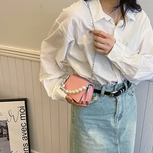 Petit sac rose avec chaîne en perles et design en accordéon sur fond de chemise blanche