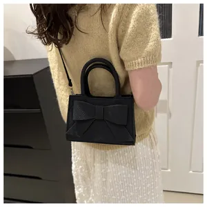 Close-up of black handbag with oversized bow detail and textured finish shown on model
