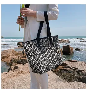 Détail du cabas en toile jacquard avec motif monogramme noir et breloque logo dorée