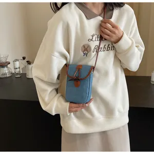 Close-up of mini denim crossbody phone bag featuring brown leather trim and horn button