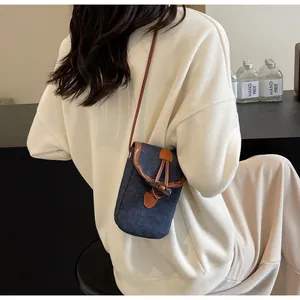Detail view of denim crossbody phone bag with horn buckle and brown leather trim on model