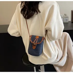 Detail of a denim crossbody bag with leather trim and vintage horn buckle on a model